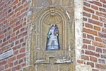 Low relief image of a begijn, one of the
					female Catholic lay members of the community holding a model of a meeting house or church in her left hand and a bible in her right,
					at an intersection.